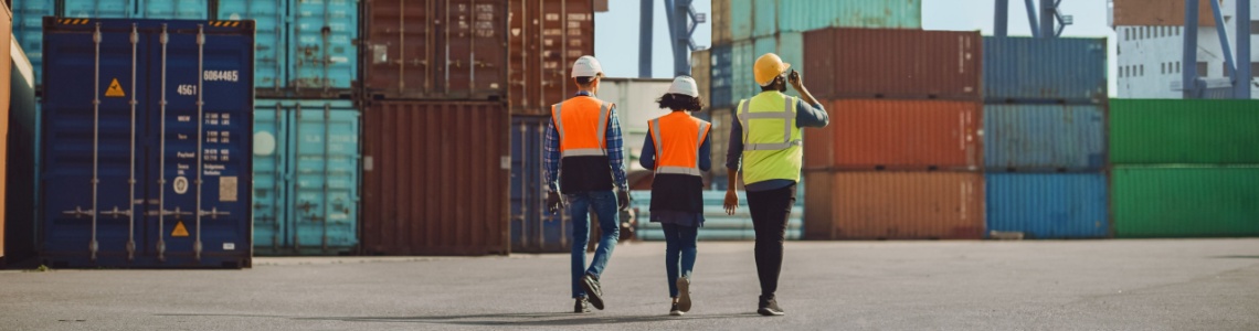 Workers walking through a shipping cargo container terminal depot.