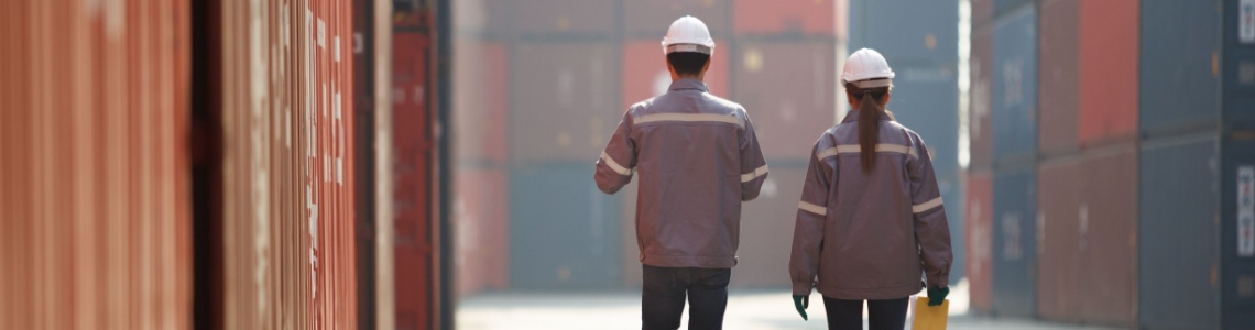 Two workers walking between shopping containers.
