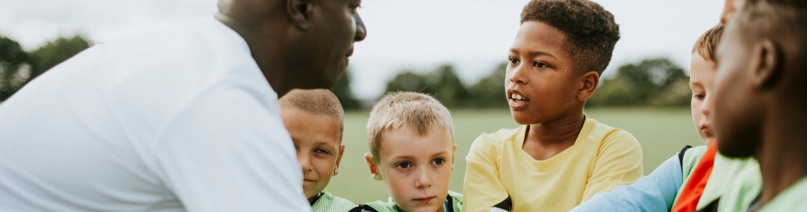 A man coaching a junior football team.