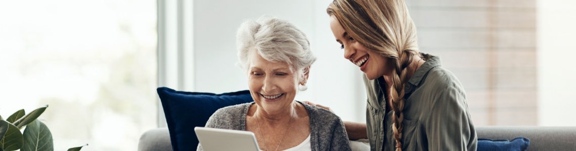 A woman showing her adult daughter something on a tablet.