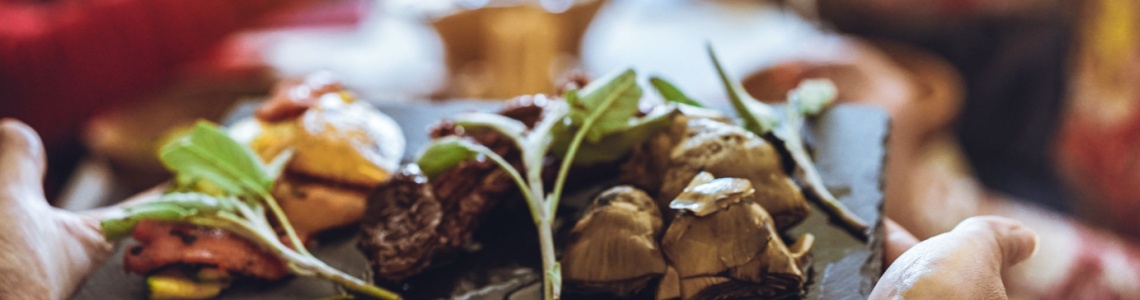 Chef bringing out platter of food, with group of people at a table in the background